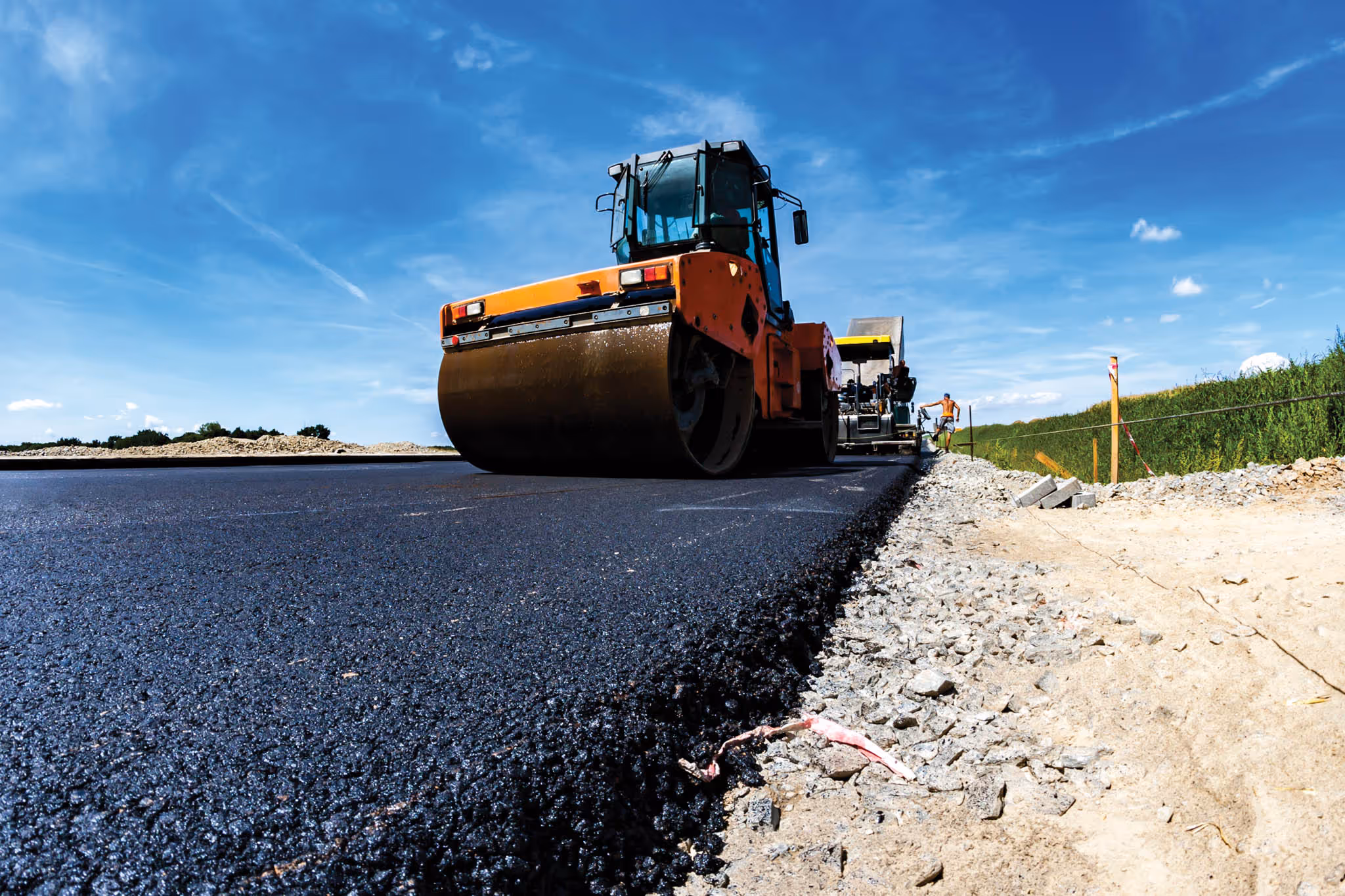 Close up of a newly paved road with a paver behind it.