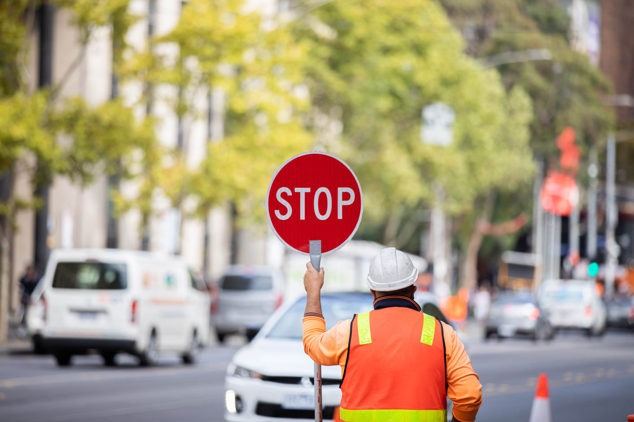 Construction worker holding up a stop sign in front of traffic on a busy road.