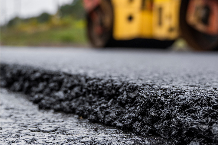 Close up of a paved road with a construction vehicle blurred in the background.