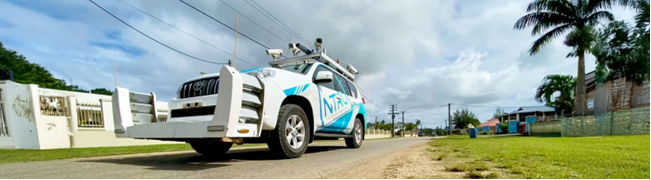 A National Transport Research Organisation (NTRO) Network Survey Vehicle (NSV) parked on a coastal road in Tonga. The vehicle is equipped with advanced survey equipment, set against a backdrop of lush greenery and a clear blue sky, showcasing the integration of technology and natural beauty.
