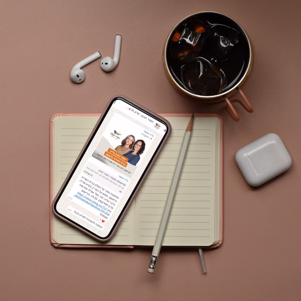 Smartphone displaying a podcast episode page on top of an open notebook, next to a pencil, wireless earbuds, and a cup of iced coffee on a brown surface.
