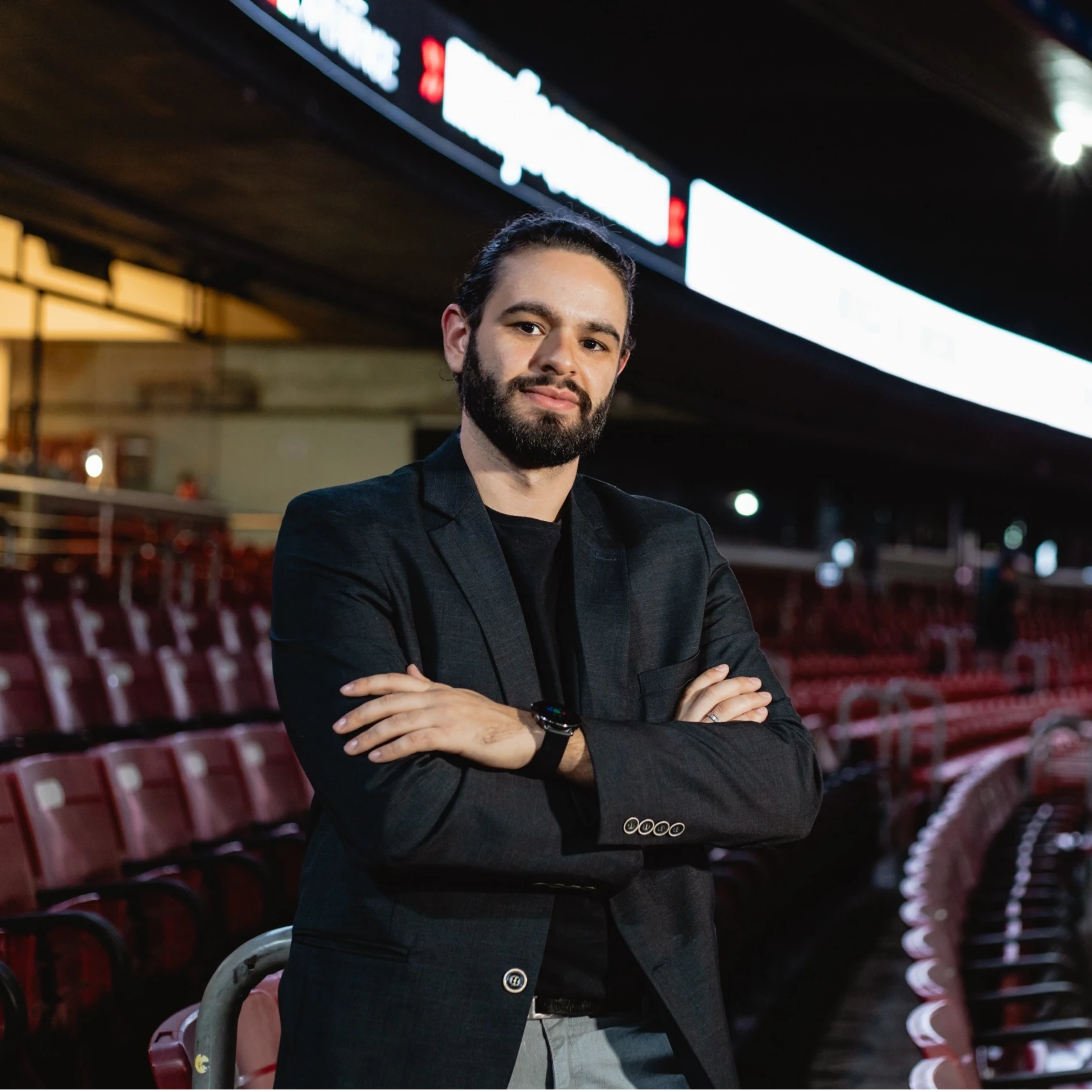 Foto em estilo retrato de José Oliver: homem branco com cabelo para trás e barba. Utilizando uma camisa preta abotoada e com os braços para baixo. Expressão serena e leve sorriso