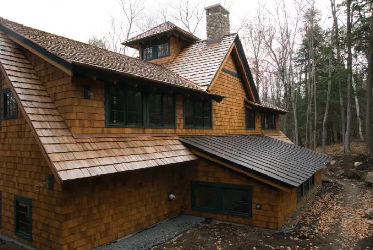 Rustic house with cedar shake siding and roof in woodland setting.