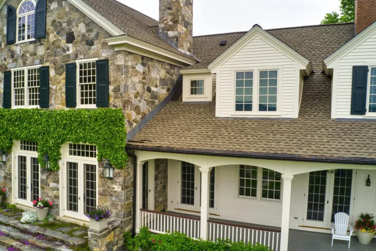 Close-up of a stone house with an elegant porch and tan roof.