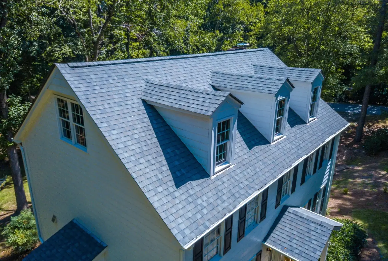 Aerial view of two-story colonial home with blue-gray shingle roof and dormers