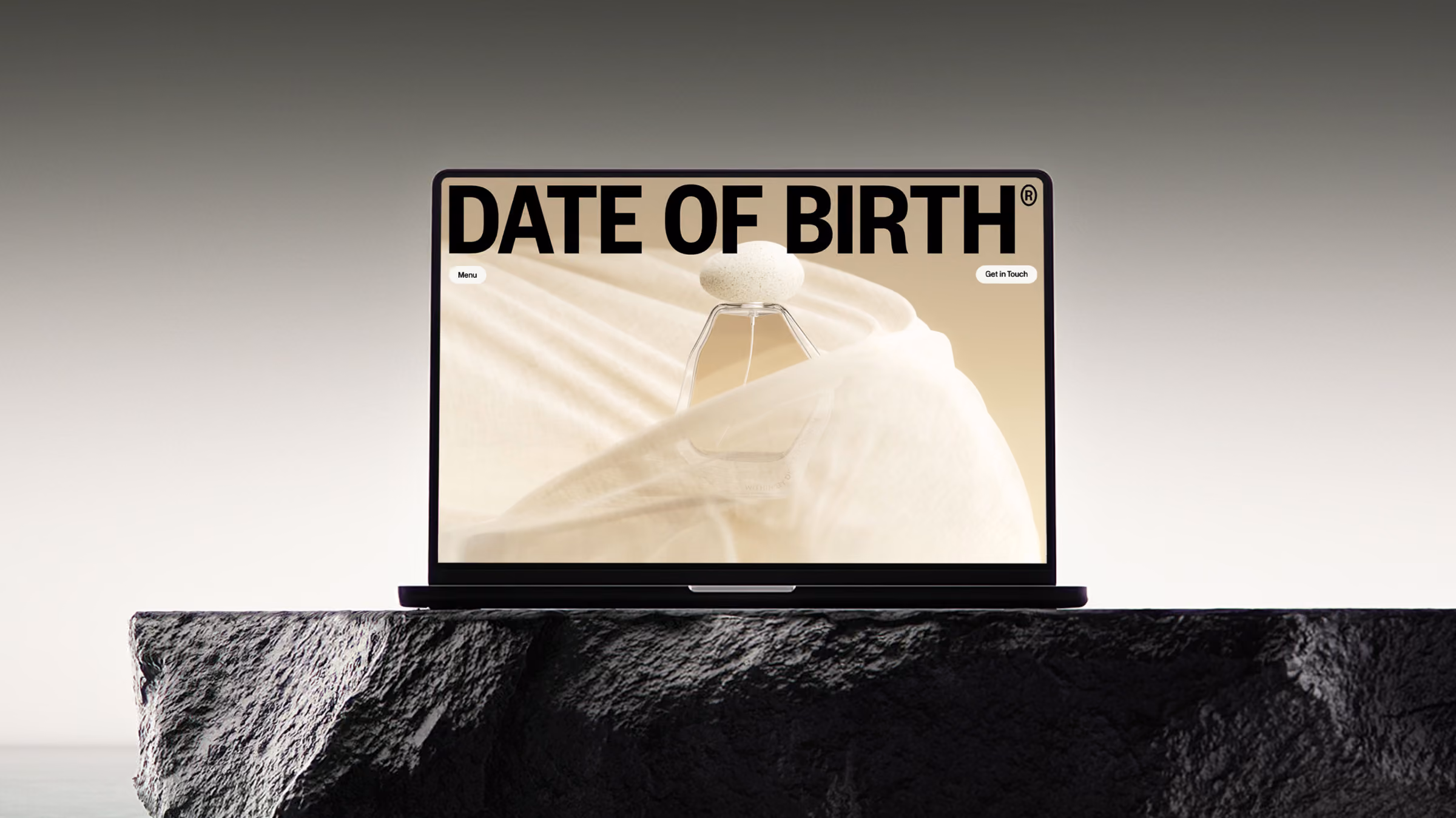 Black laptop placed on a rough textured dark stone surface, displaying a screen with the words 'DATE OF BIRTH' in bold uppercase letters against a creamy beige background with an abstract architectural structure.
