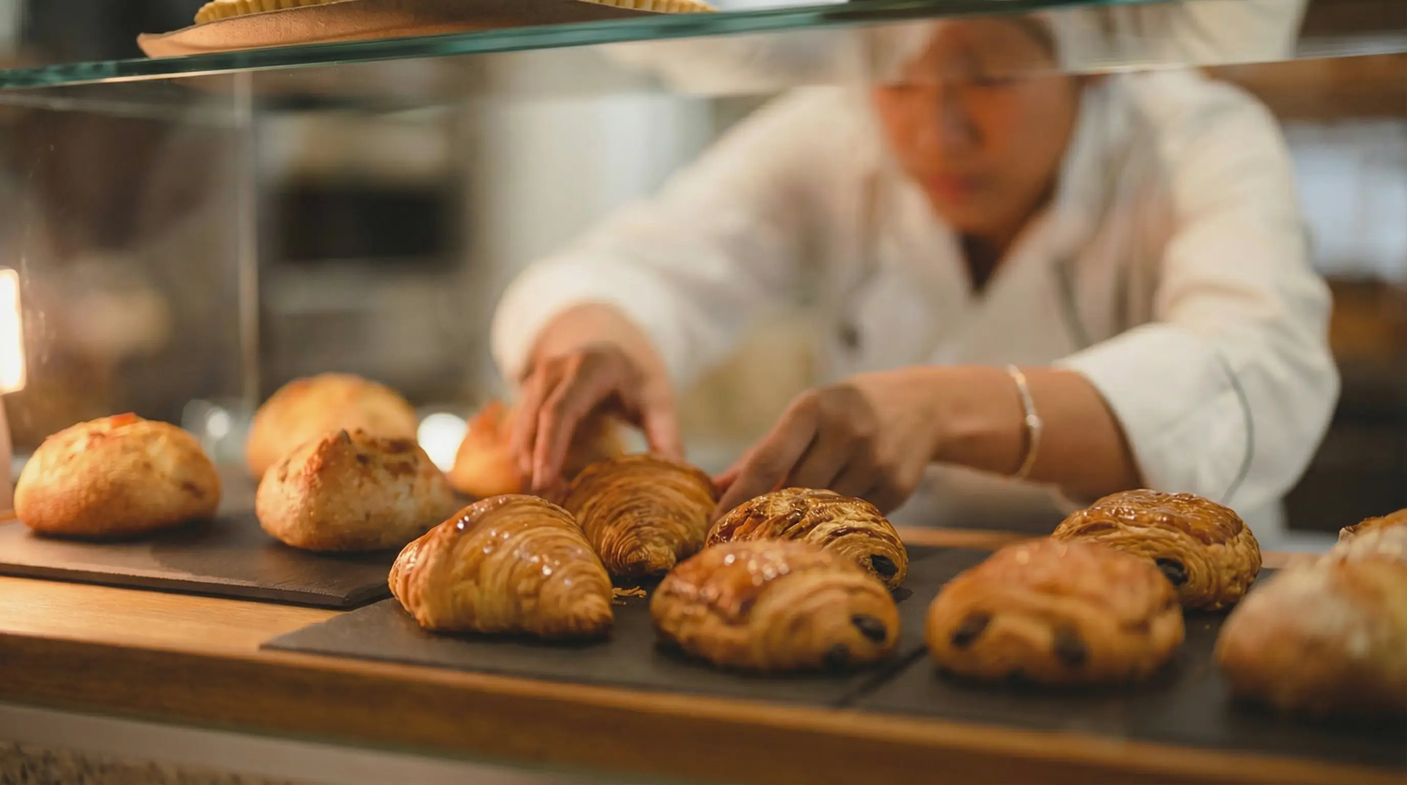 Boulangère disposant des viennoiseries en vitrine dans une boulangerie-pâtisserie