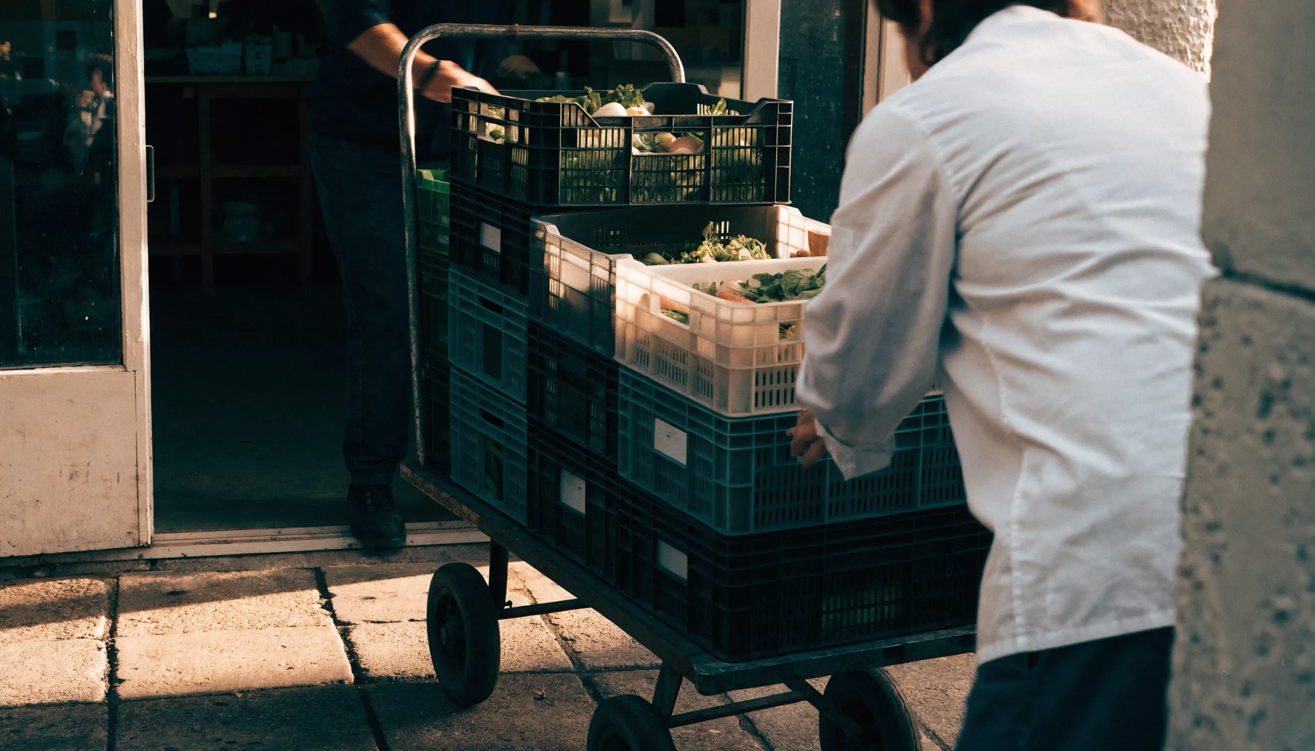 Réception d'une livraison fournisseur à l'arrière d'un restaurant, cagettes de légumes frais empilées sur un diable
