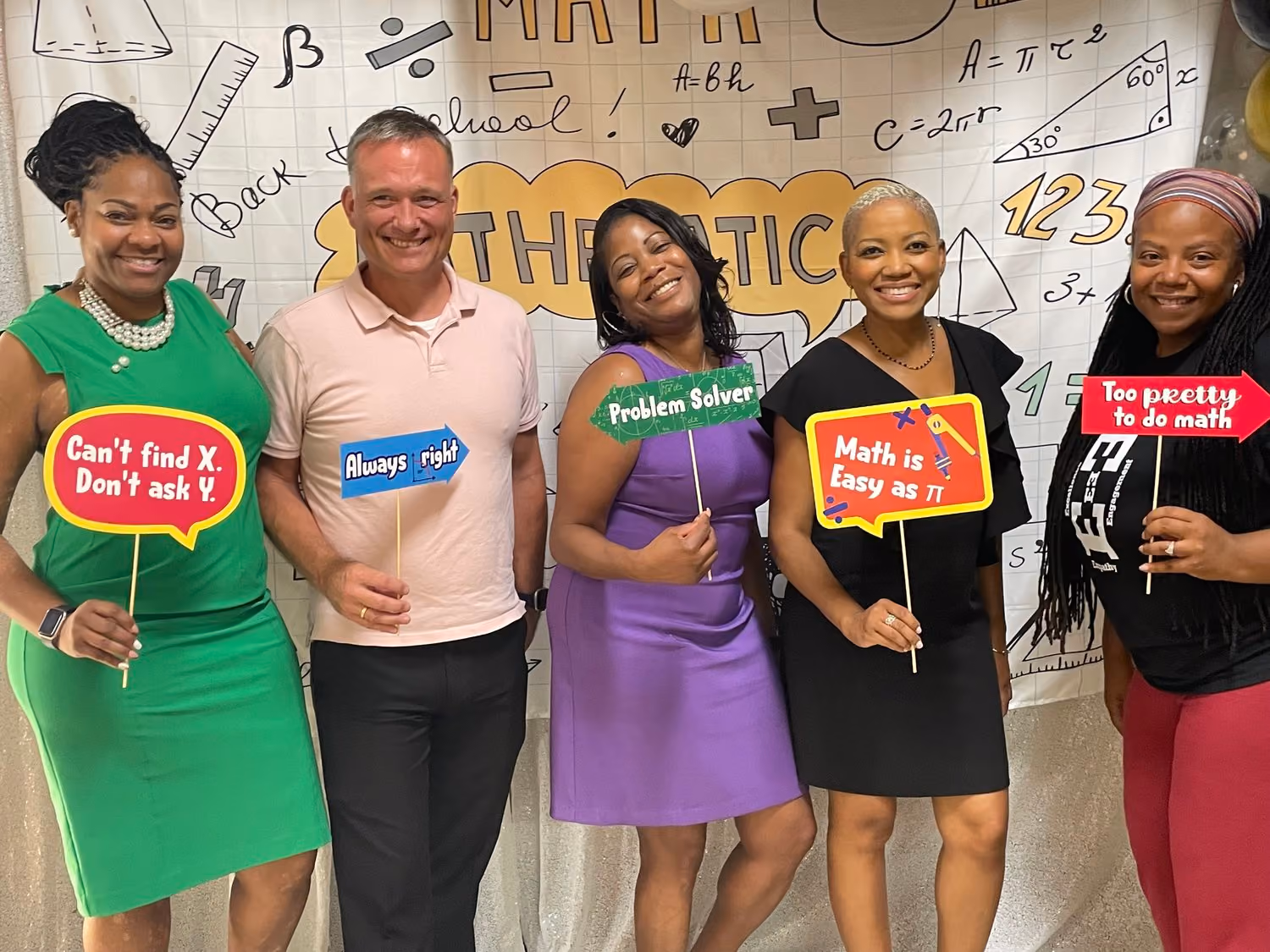 Five staff members pose with math-themed signs at school event