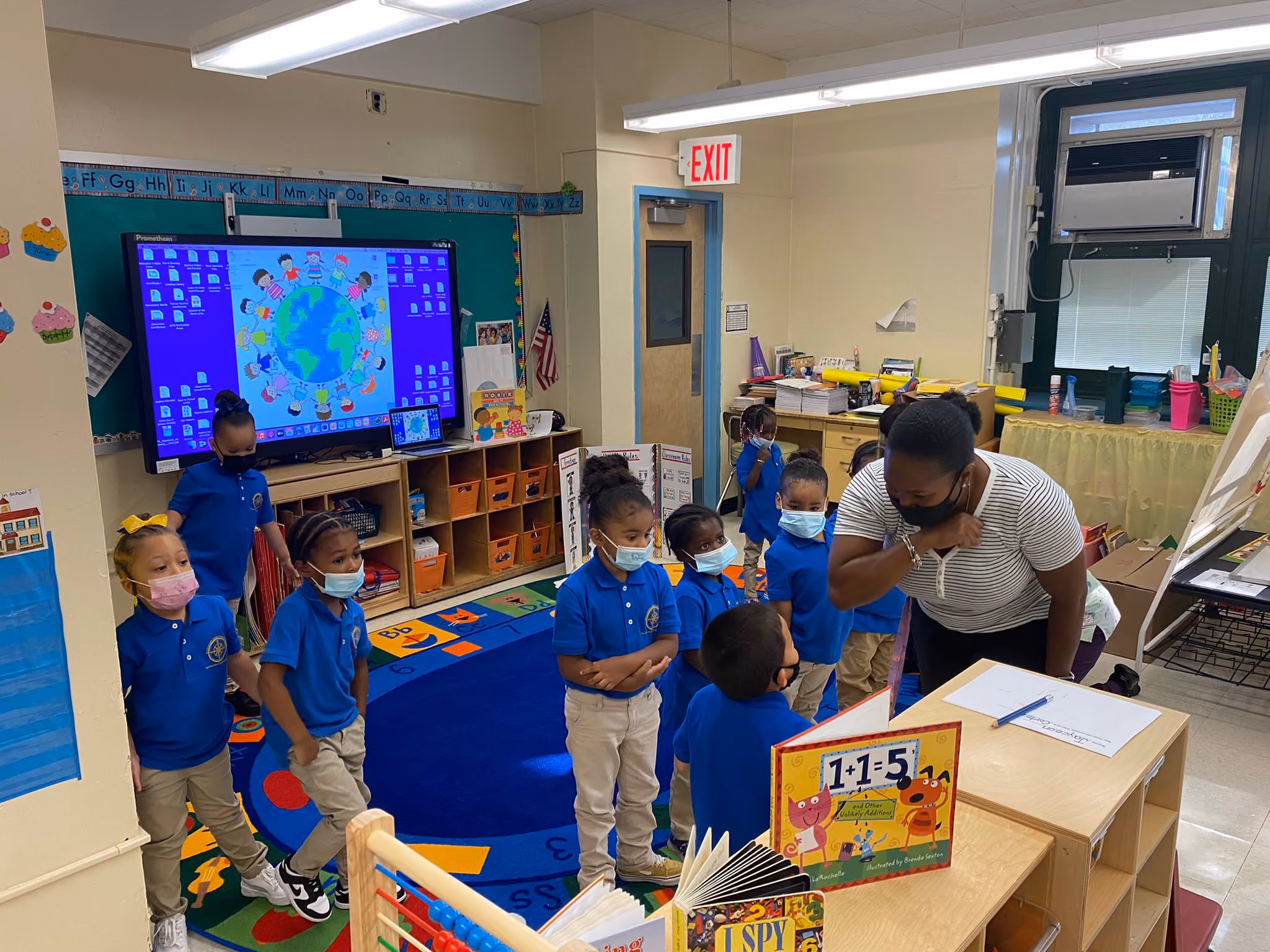 Teacher and masked kindergartners gather during a classroom reading lesson