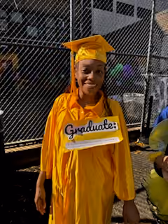 Student in yellow graduation cap and gown holding Graduate sign