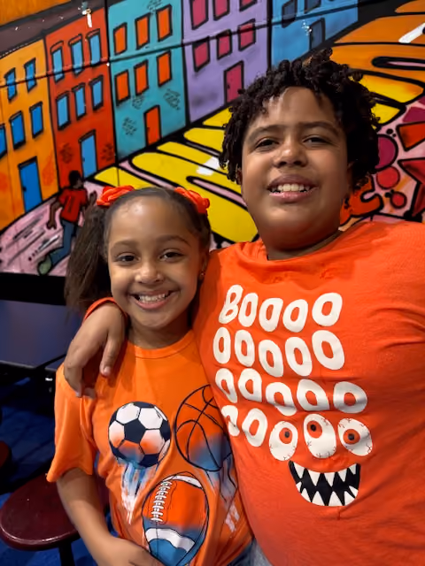 Two smiling students posing in front of colorful school mural