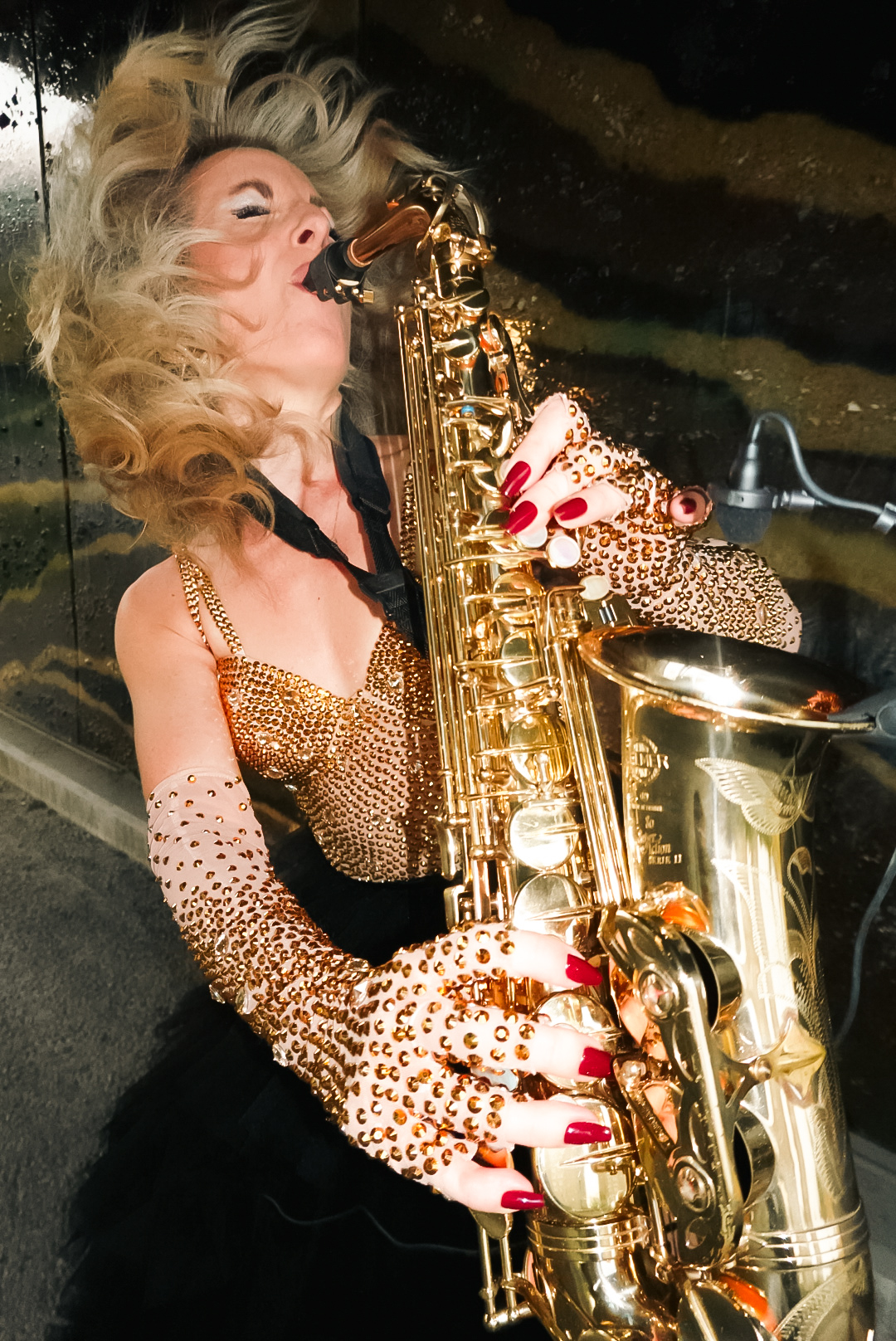 Sheona Urquhart Smångs in a gold, rhinestone leotard, playing a saxophone