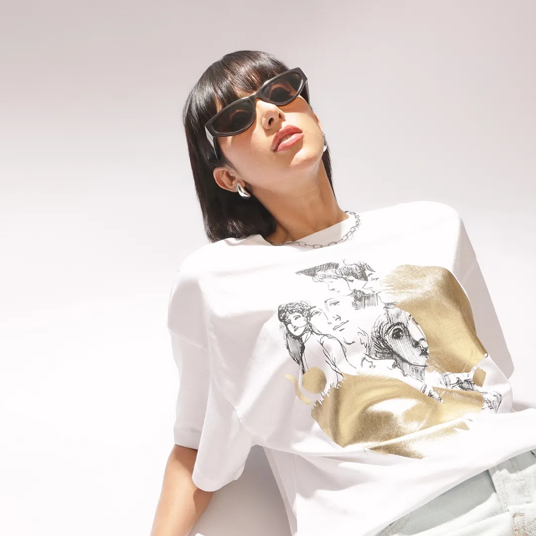 Female model in an oversized white graphic t-shirt with gold accents.
