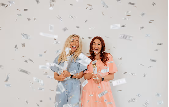 Two women celebrate with money confetti.