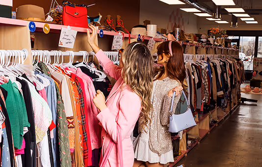 Two women browse clothing racks at a Indy Clover thrift store.
