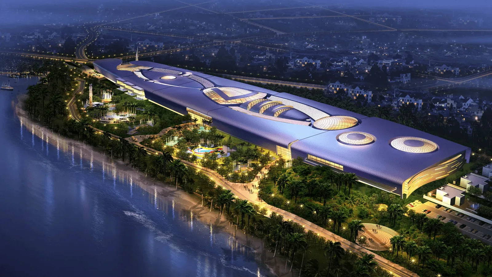 A large, modern building with a unique, curved roof is situated near a river, surrounded by gardens and walking paths. The area is illuminated at night, showcasing its vibrant landscape.