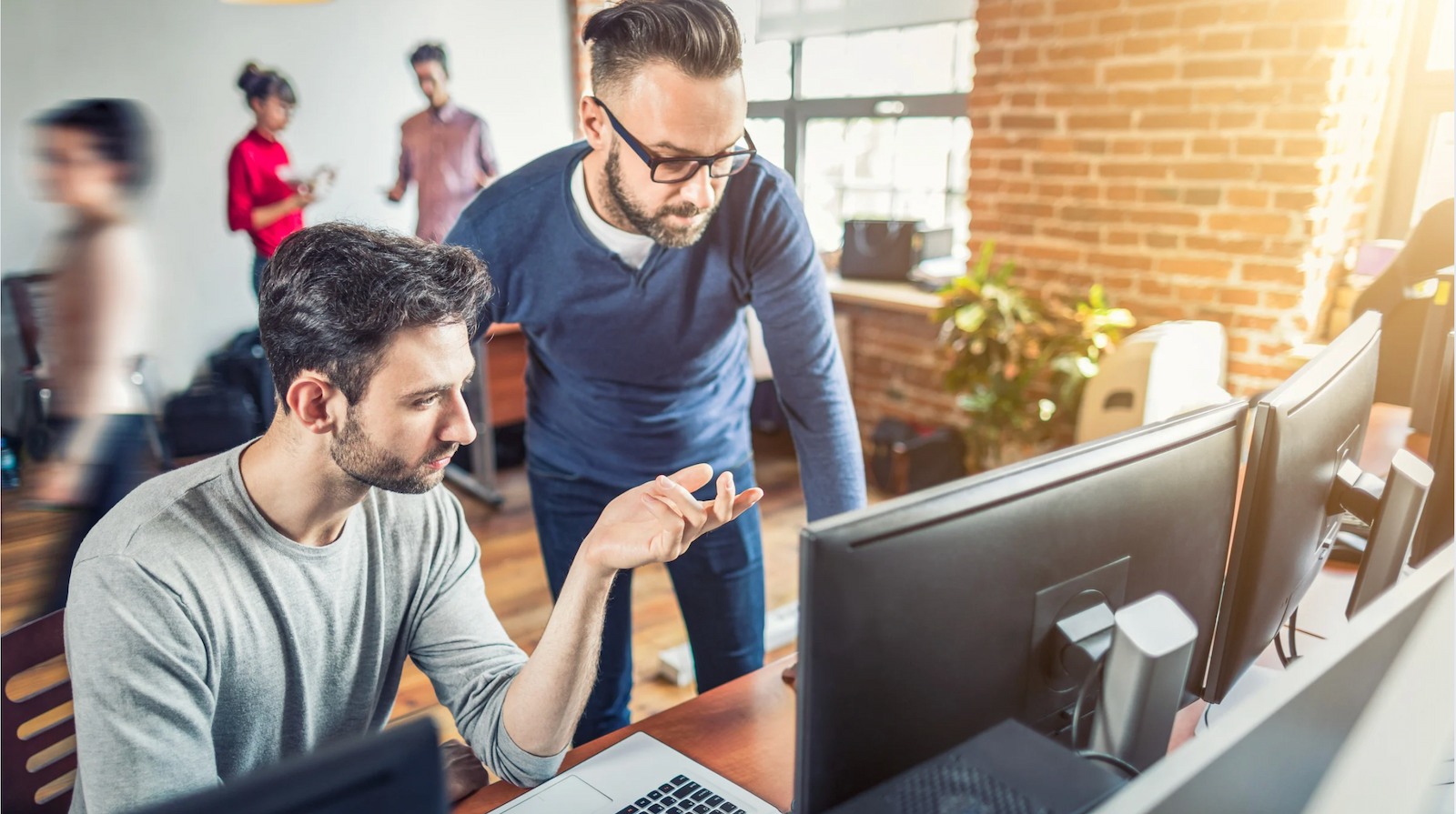 two male senior software developers looking at computer screens in a busy office