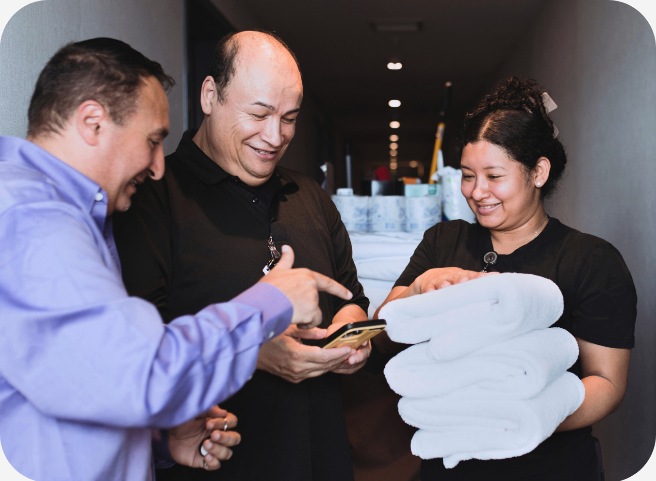 Hotel staff reviewing a task on a mobile device while coordinating guest service and housekeeping responsibilities in a hotel hallway.
