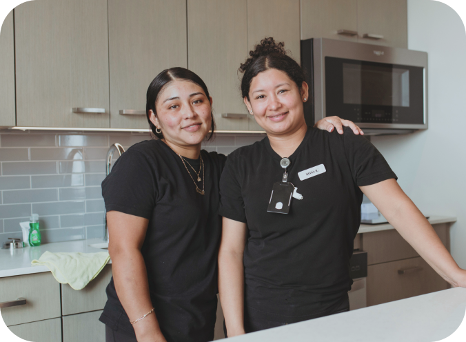 Two housekeeping employees standing together in a hotel guestroom.