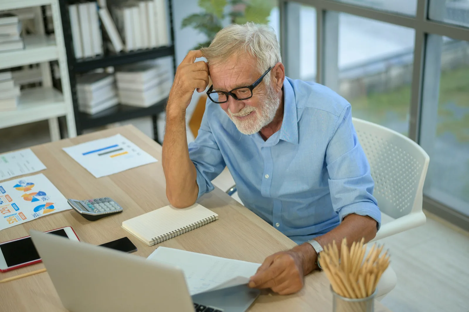 Un dirigeant analyse des graphiques imprimés à son bureau, calculatrice et ordinateur portable à portée de main.