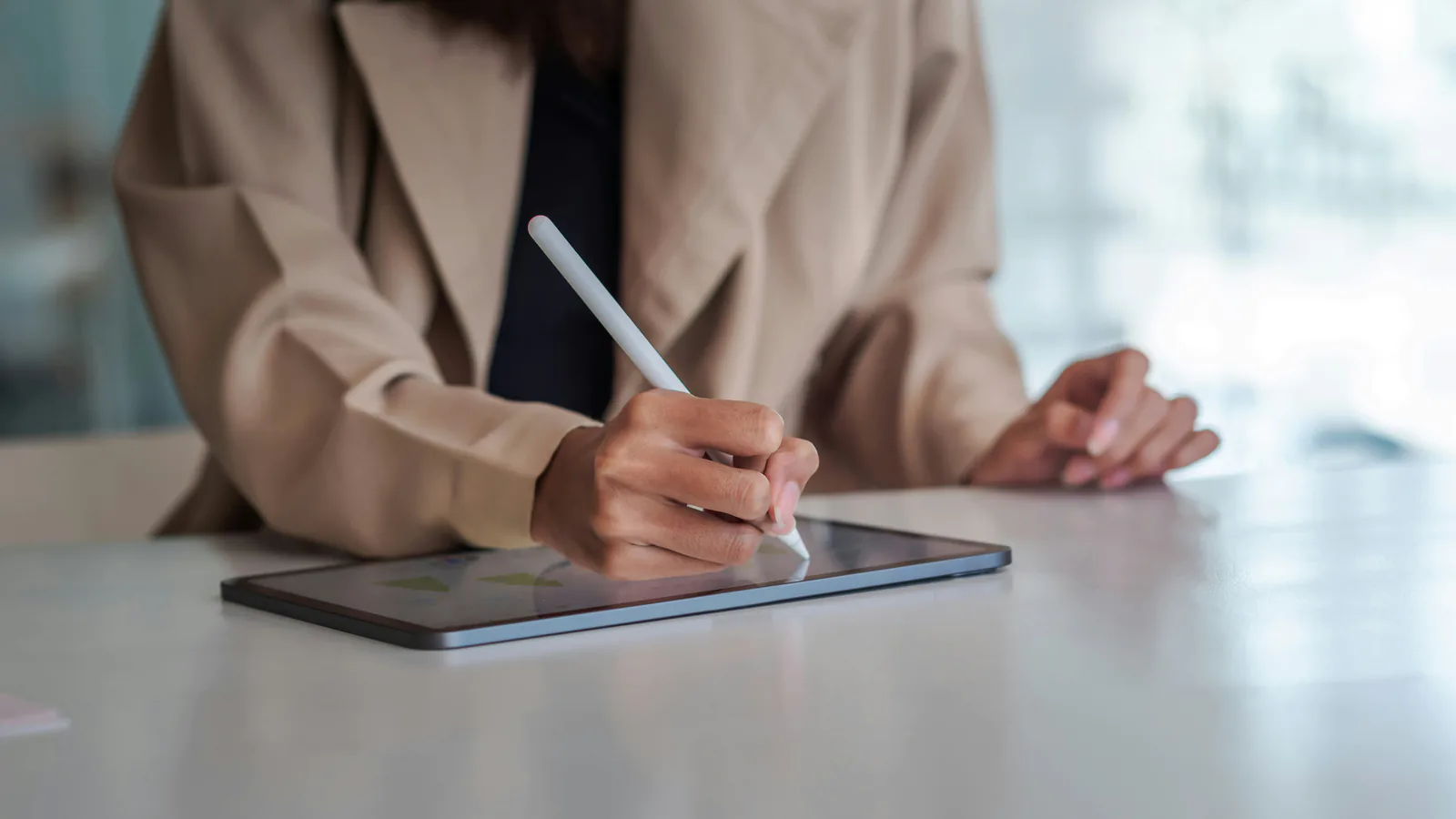 Une professionnelle signe un document sur une tablette avec un stylet, à son bureau.