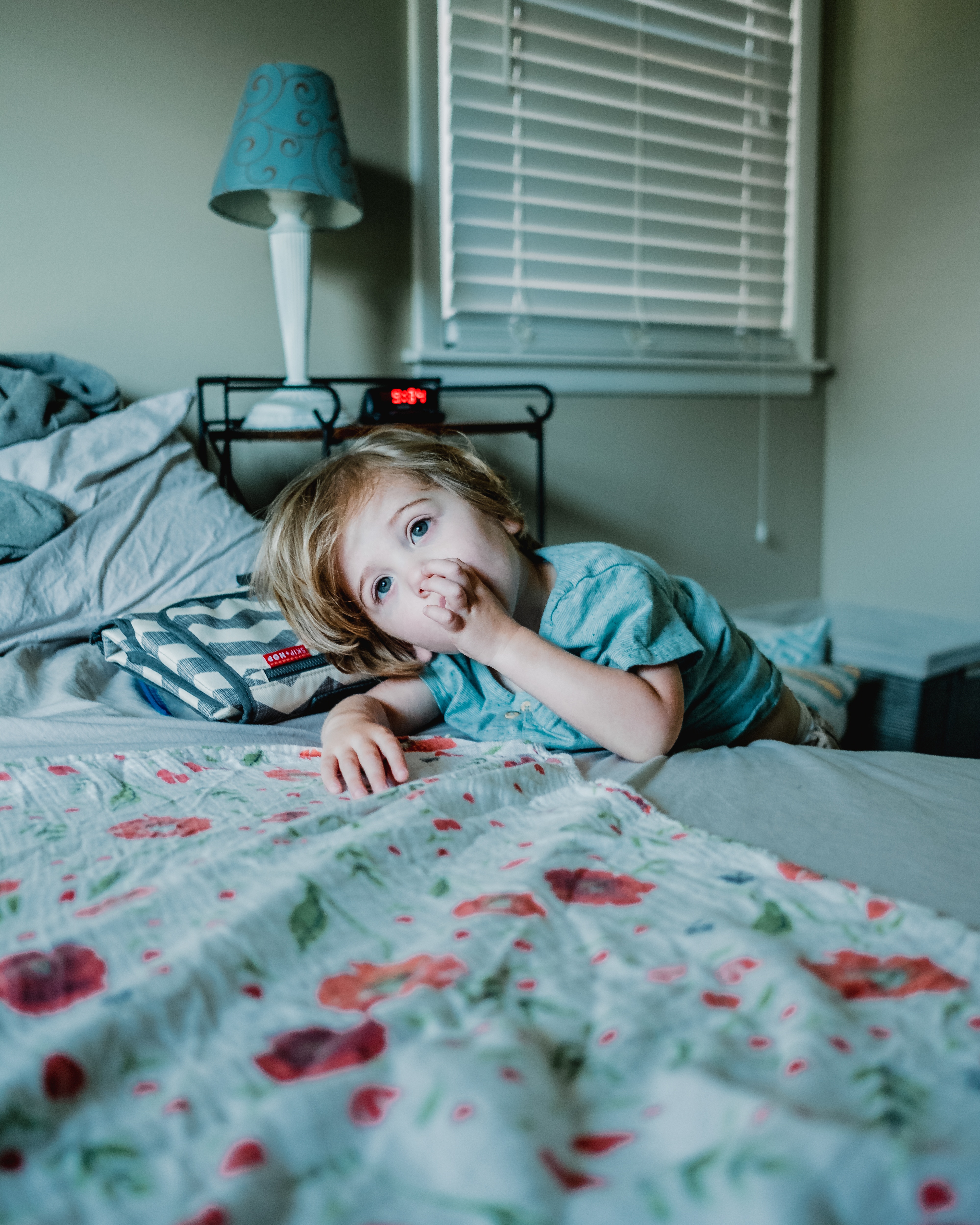 A child sits on a bed and sucks their thumb. Thumb-sucking can lead to dental issues, so it's important to break the habit.
