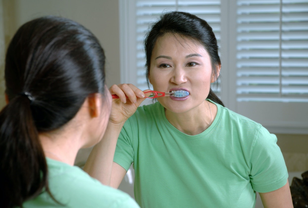 A woman looks in the mirror as she brushes her teeth.