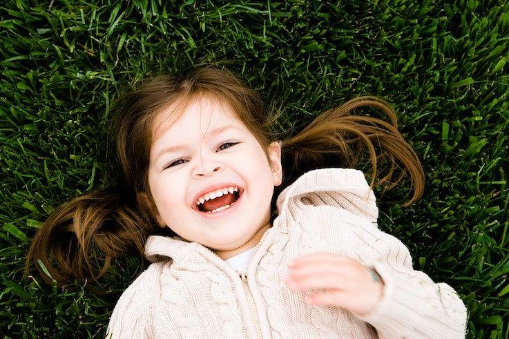 A young girl lays in the grass and smiles up at the camera