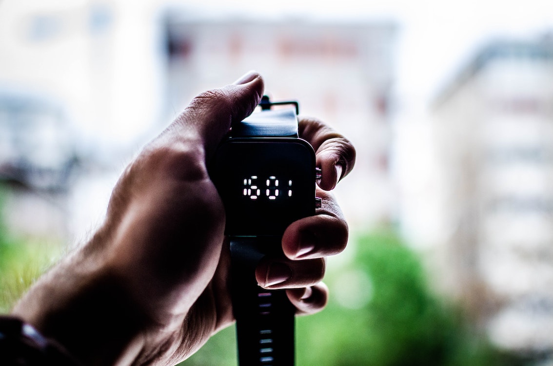 A hand holds up a smart watch displaying the time.