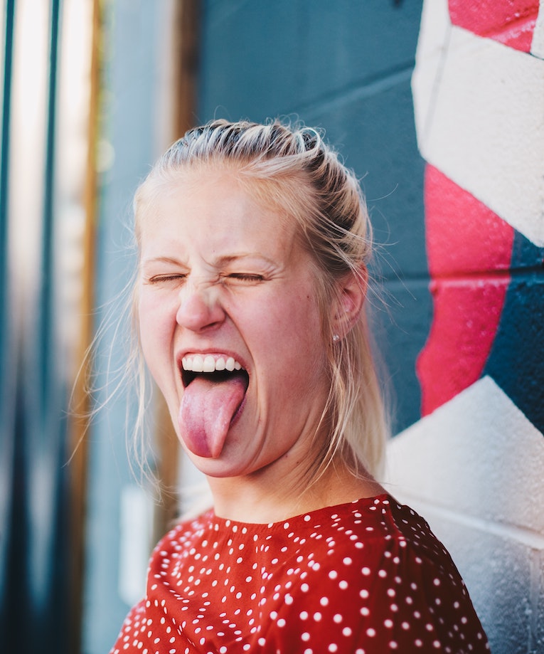 A woman in a red polka dot dress closes her eyes and sticks her tongue out.