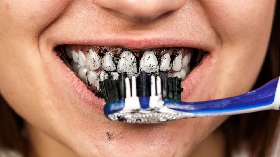 A close-up photo of a child brushing their teeth with charcoal toothpaste