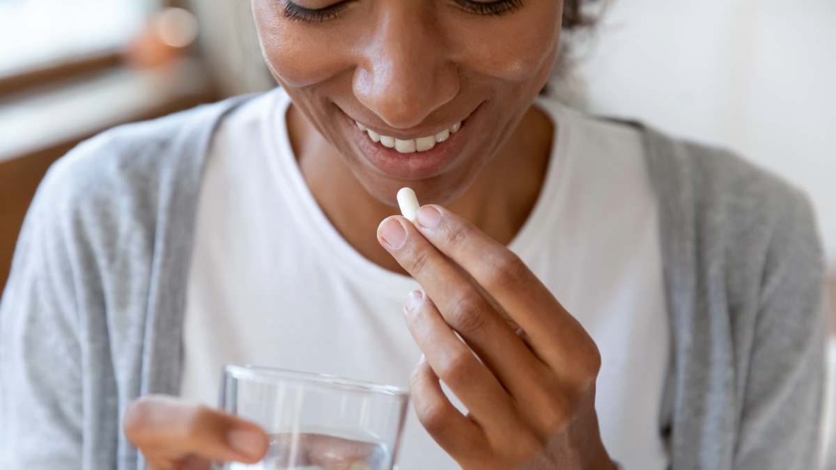 A woman taking a probiotic pill with a glass of water