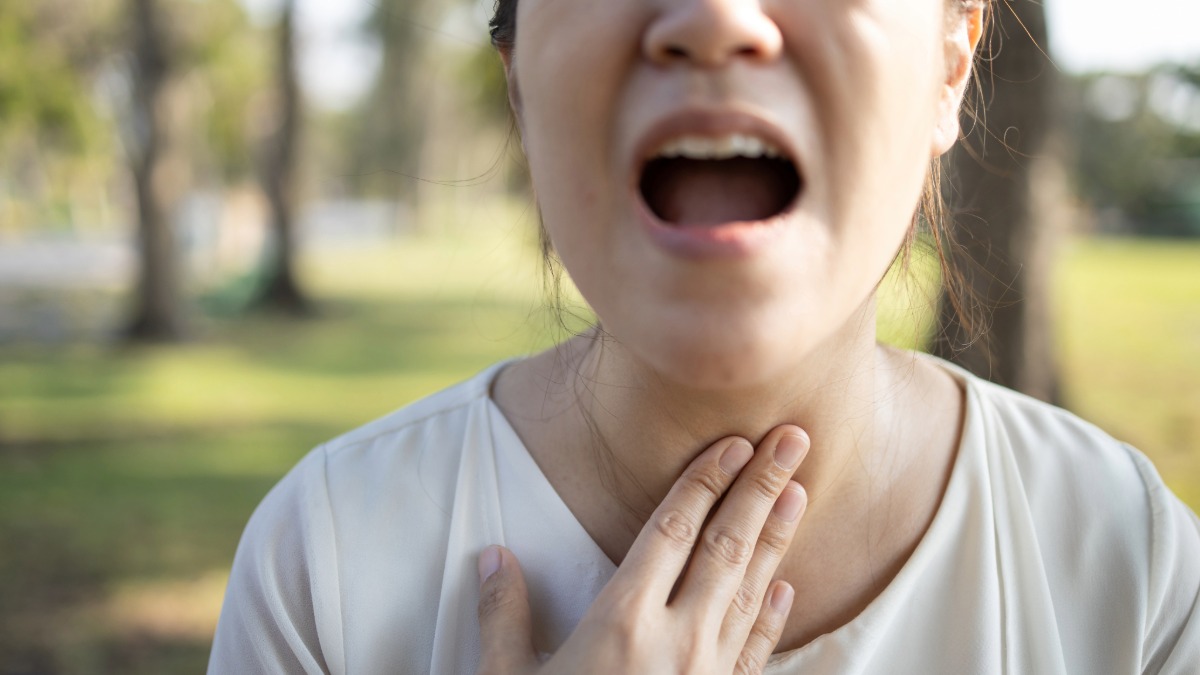 An out-of-focus women looking pained and holding her throat