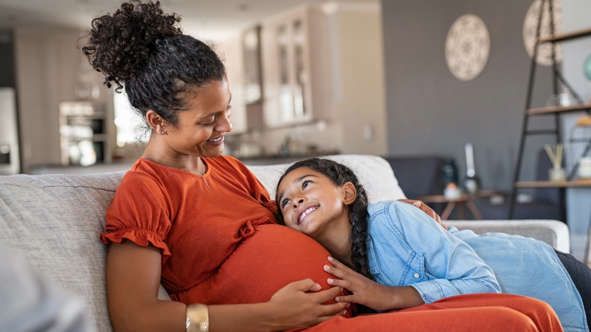 An expectant mother being hugged by her smiling child