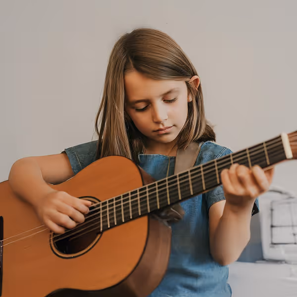 Young girl with straight brown hair playing an acoustic guitar indoors.