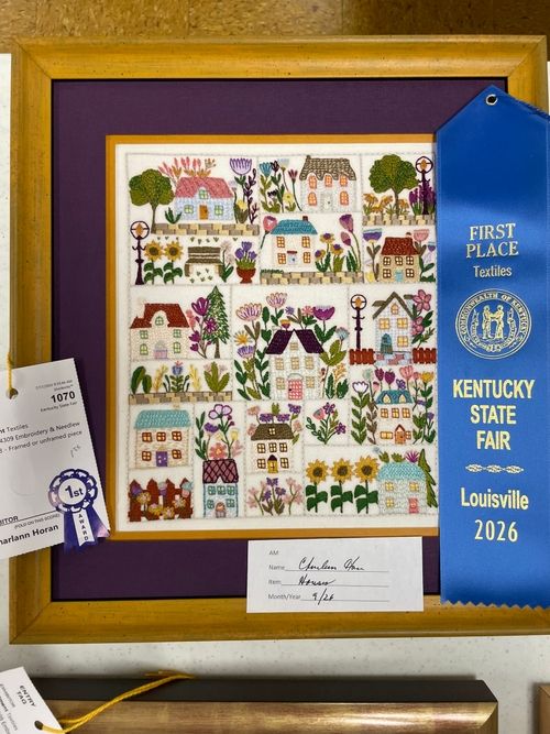 Framed sampler of houses and gardens with a first place Textiles ribbon
