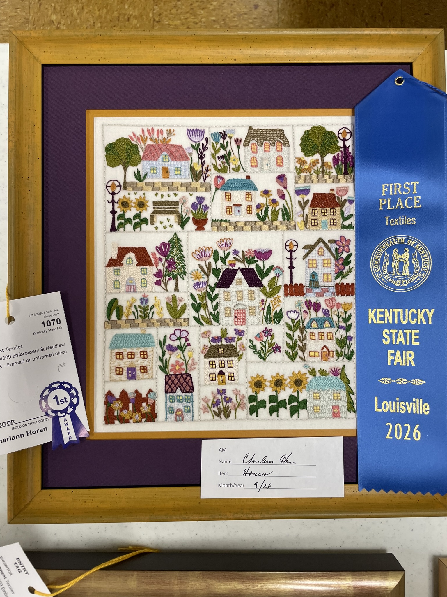 Framed sampler of houses and gardens with a first place Textiles ribbon