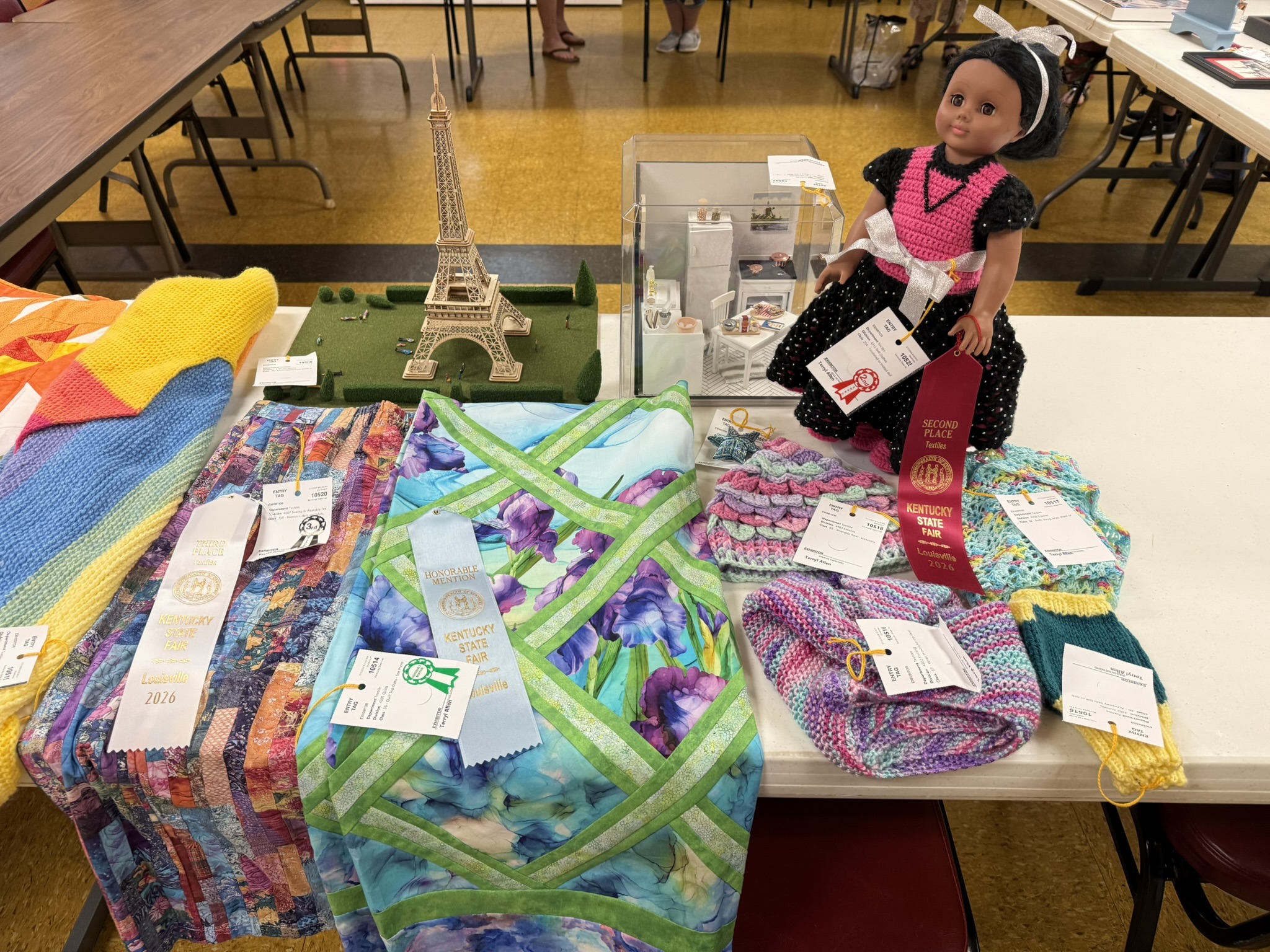 Kentucky State Fair display table with quilts, a stitched Eiffel Tower and a doll in a hand-stitched dress