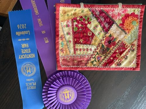 Crazy quilt block in reds and golds with a first place ribbon and Best of Show rosette