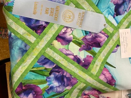 Quilt in purple and teal florals with a green lattice pattern and an honorable mention ribbon