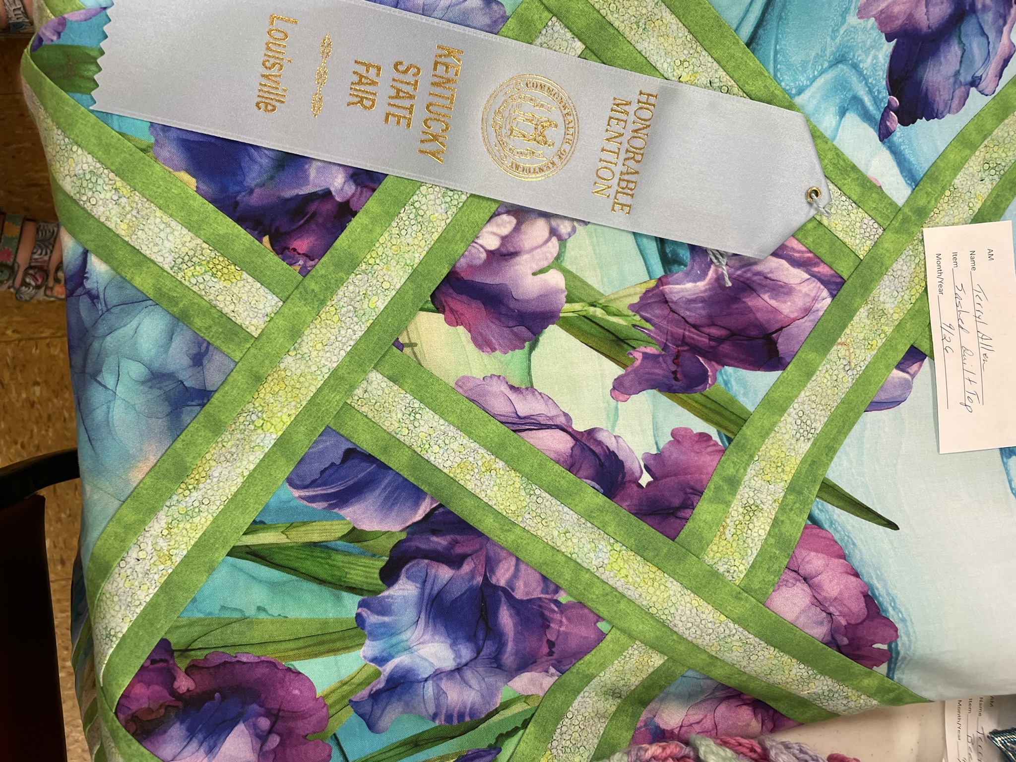 Quilt in purple and teal florals with a green lattice pattern and an honorable mention ribbon