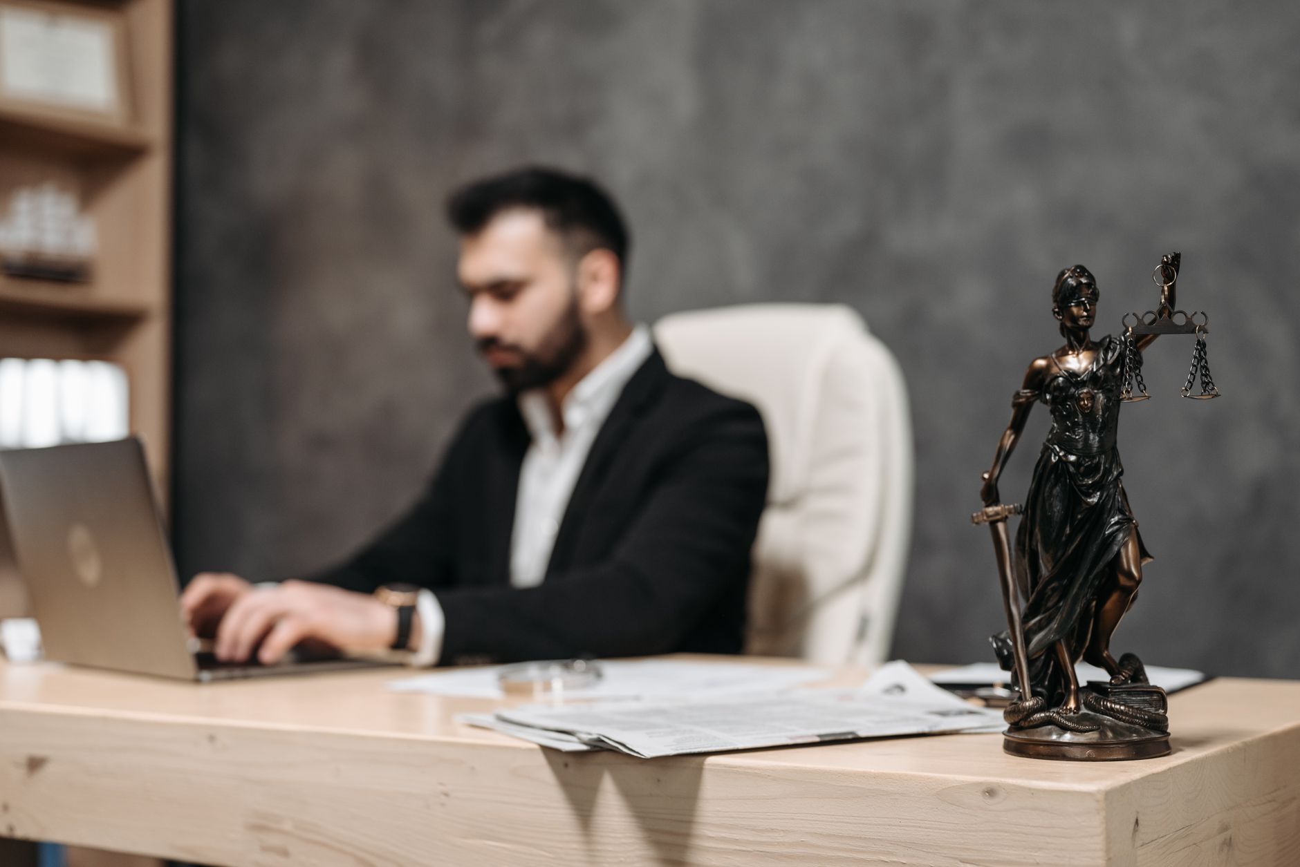 Businessman working at a laptop with a Lady Justice statue on the desk, reflecting the reality of AI in law versus vendor promises.
