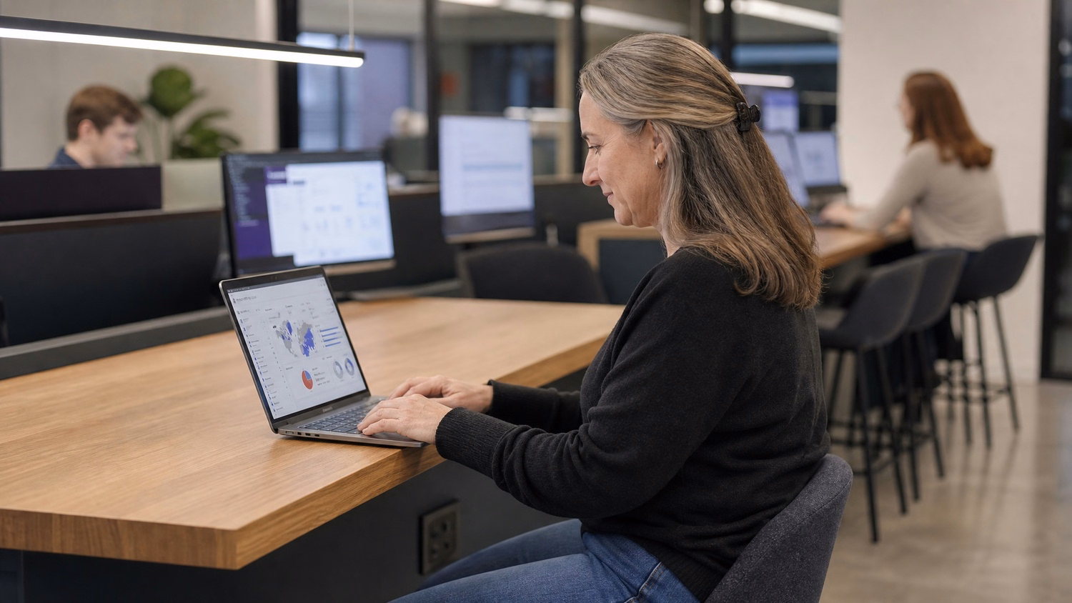 Woman at bar-height desk types on laptop, viewing login data