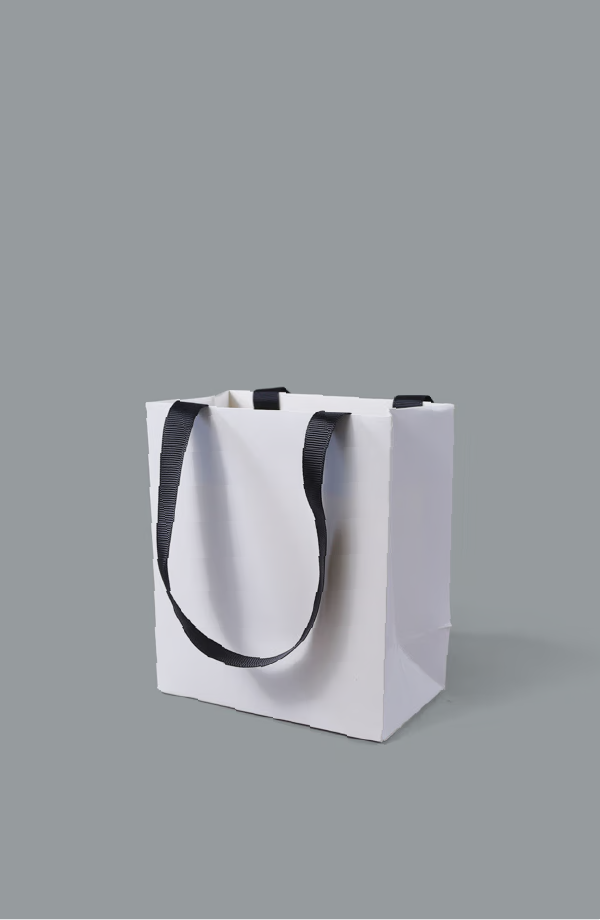 White paper bag with black woven webbing handles, shown with the gusset and base folds visible