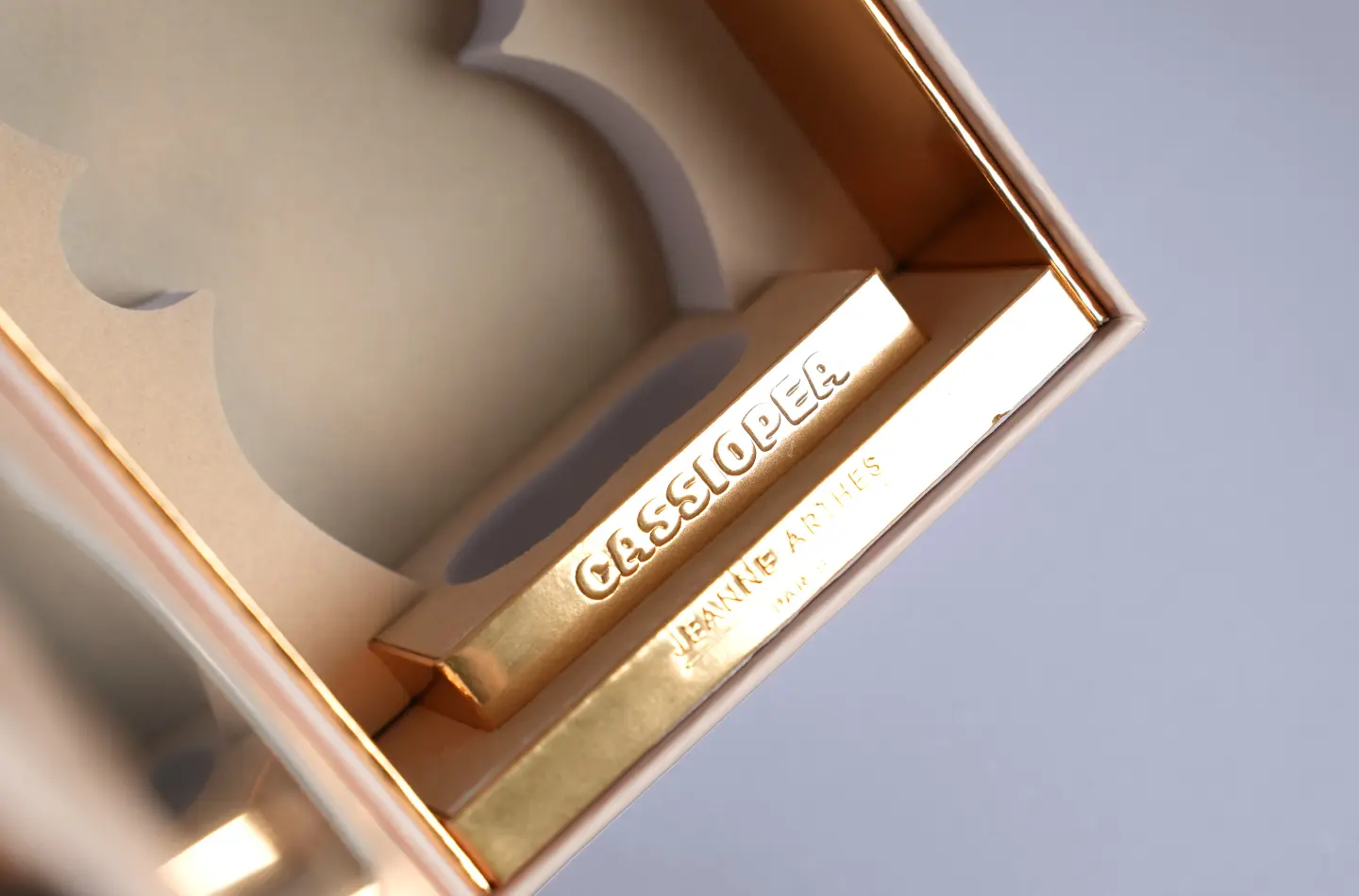 Front-facing display of an opened luxury perfume book-style box featuring gold stamping and a window cutout