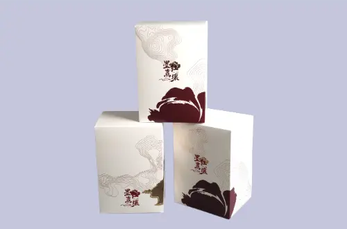 Three custom embossed tuck boxes stacked together, showing red-gold foil details and front window openings