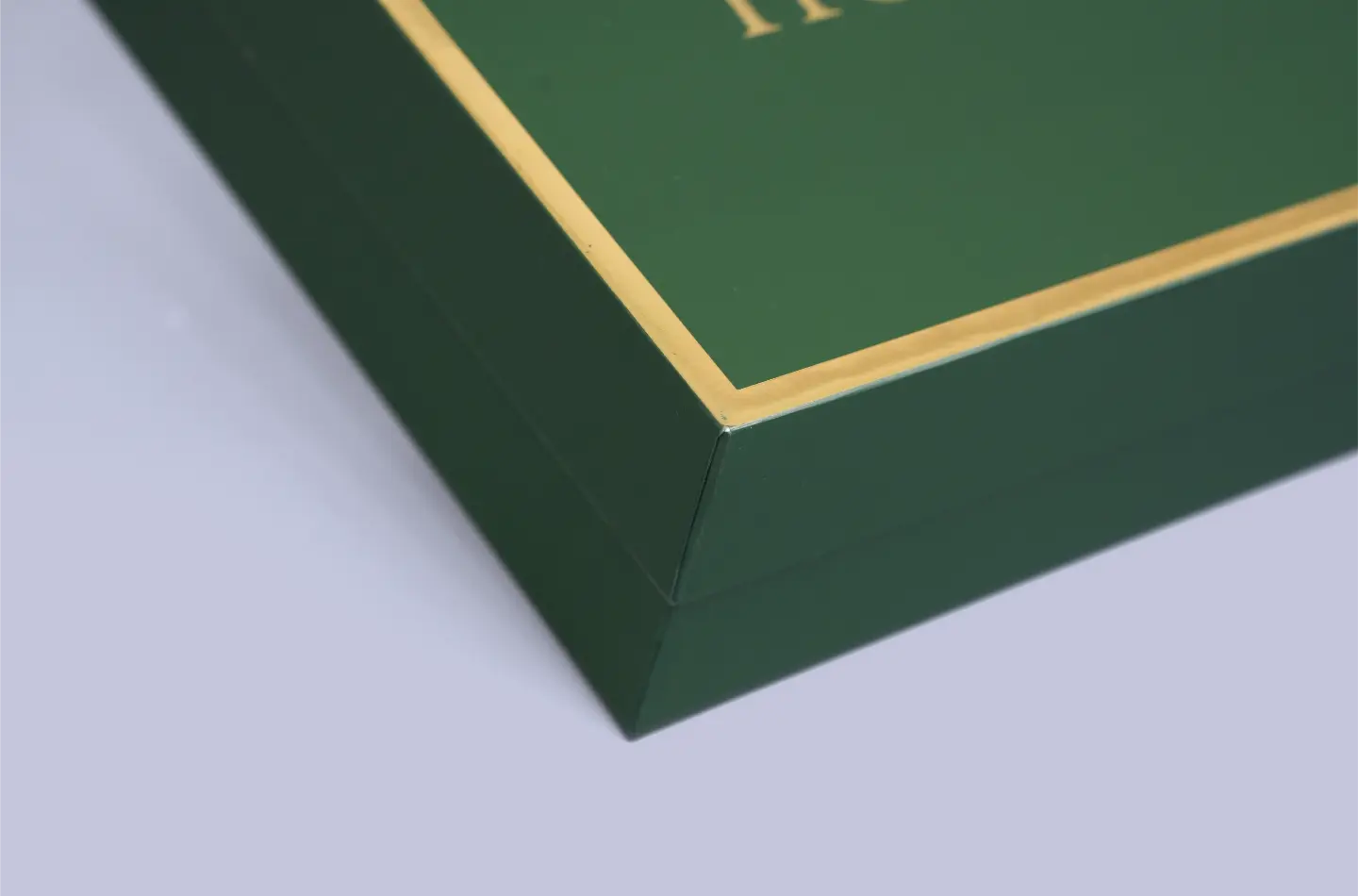 Detailed corner close-up of a high-end green rigid lid-and-base packaging box featuring metallic gold hot stamping
