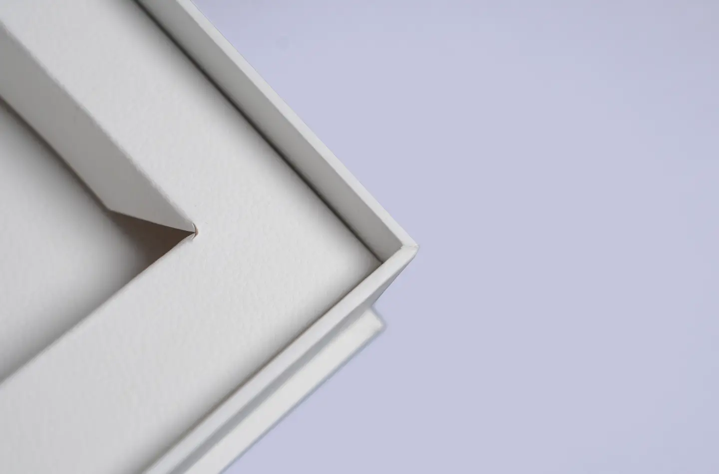 Detail shot from above of the interior corners and edges of an opened white book-shaped box with textured surface and inner lining