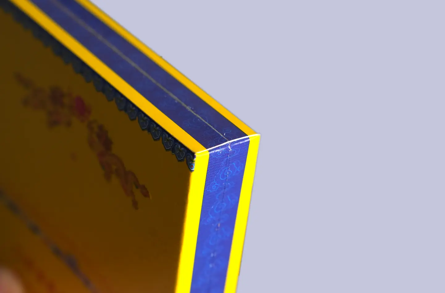 Detailed view of the outer surface of a gold flip-top paperboard box featuring embossing and UV print